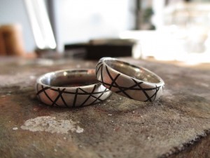 Silberne Ringe mit einer gebürsteten Textur, durchbrochen von netzähnliche, schwarzen Einkerbungen.