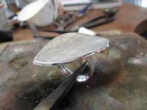 Ein silberner Ring mit einer konkaven Front in Form eines Blattes.