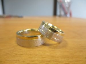 Silberne Ringe mit gebürsteter Textur und einem gedrittelten Rücken entlang der Länge des Rings. Die rechten zwei Drittel sind Gold an Stelle von Silber.
